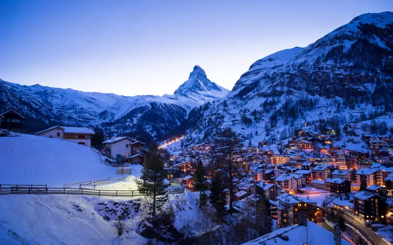 An evening view of Zermatt with the Matterhorn and village lights reflecting off the snow