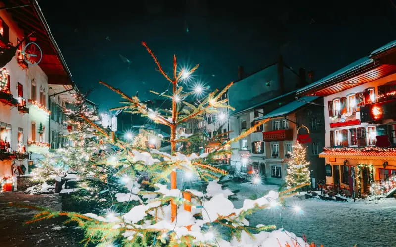 Snow-covered Christmas tree sparkling with lights in a Swiss village street