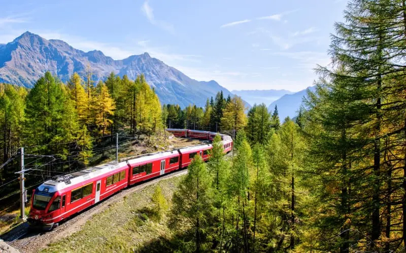 A red Swiss train winding through mountain forests under a blue sky